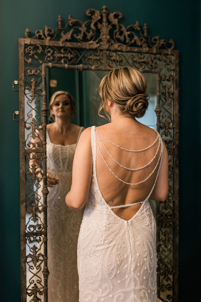 back of bride wearing detailed beaded wedding dress with low back and her hair worn in a low, intricate bun