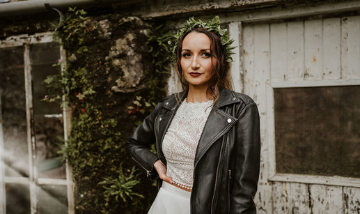 Bride wears black leather jacket over her dress and green foliage hair accessory