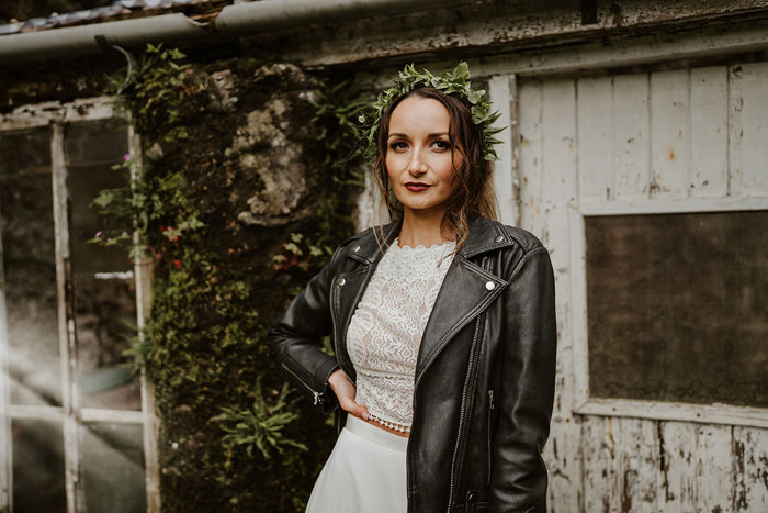 Bride wears black leather jacket over her dress and green foliage hair accessory