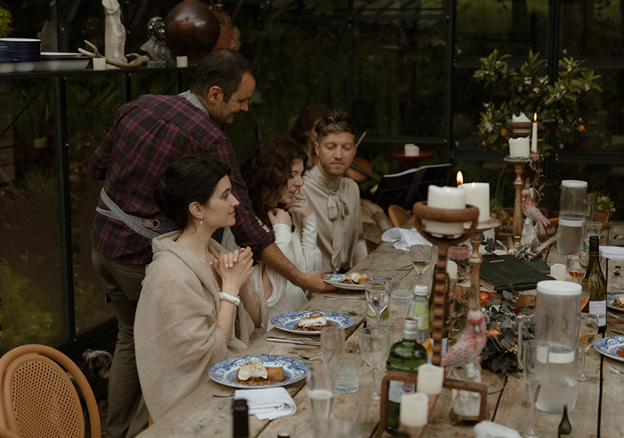 people seated for dinner around a large wooden table while a person serves food on blue and white plates