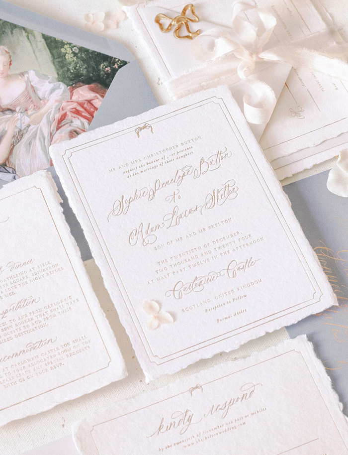 an overhead image of formal invitations on thick white paper with golden calligraphy