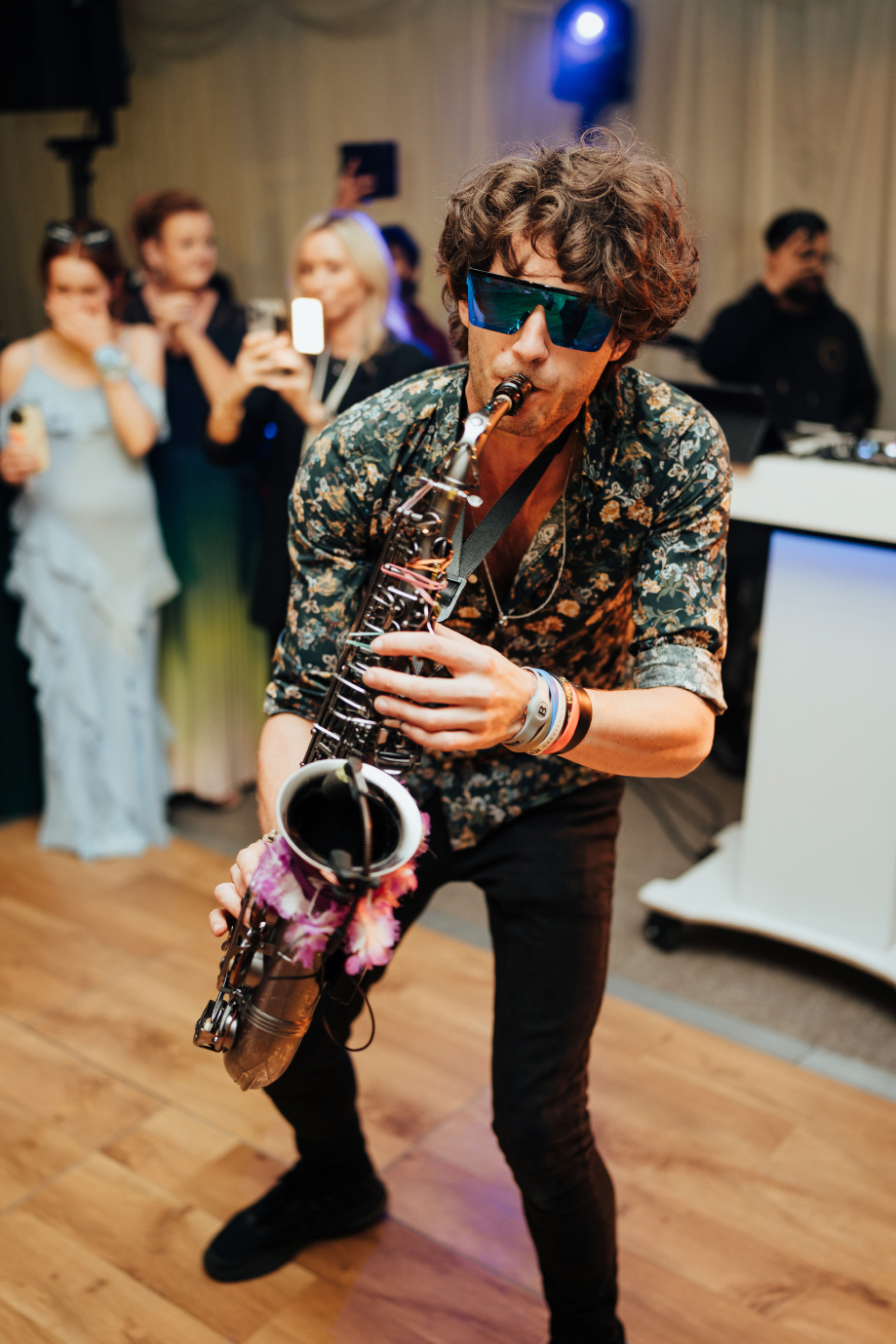 A man wearing sunglasses and playing a saxophone on a dancefloor