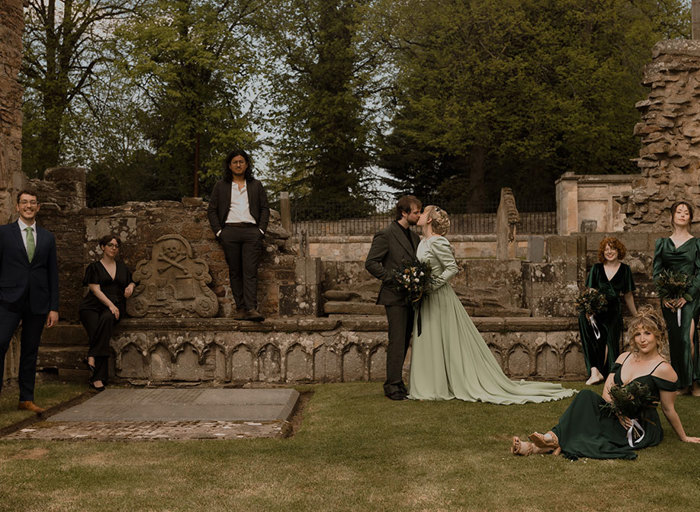 a wedding group posing in the graveyard at Elgin Cathedral as bride and groom kiss