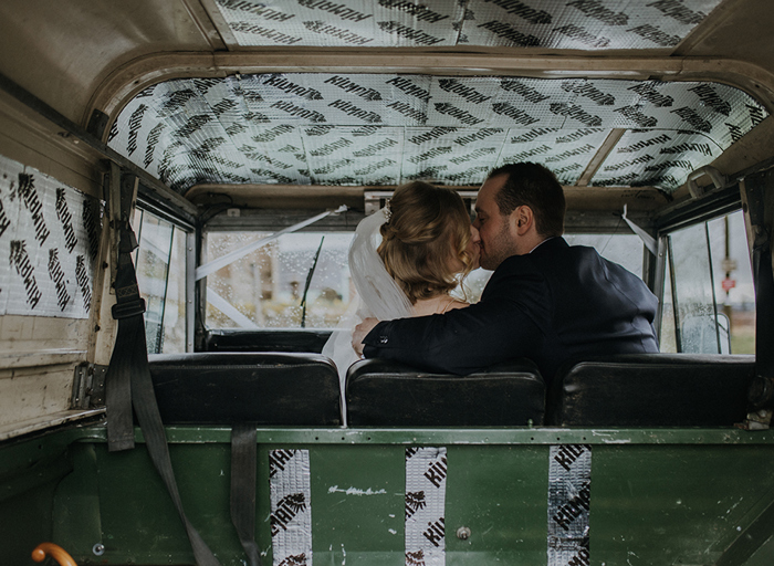 Looking from the back of a jeep into the front seat where a couple kiss 