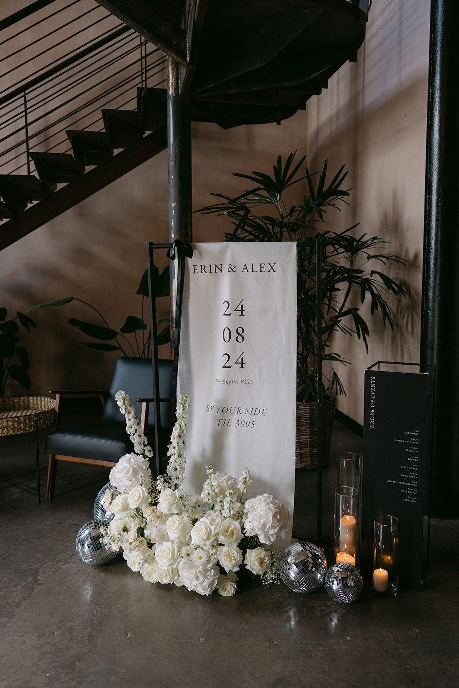 a black and white welcome sign at a wedding with white flowers, candles and disco balls.