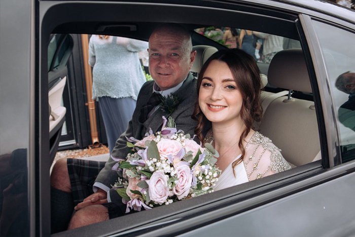 A Smiling Bride Holding A Bouquet Sitting Next To A Man In The Back Of A Black Car