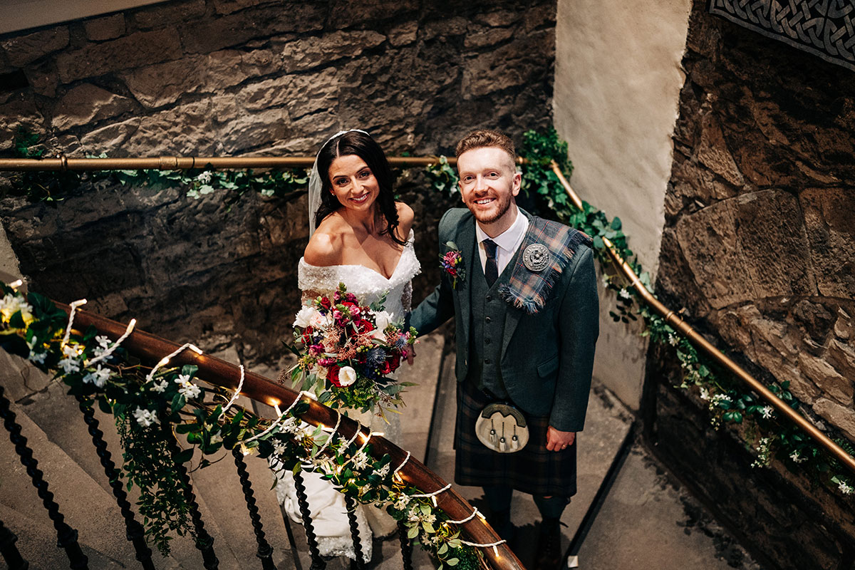 bride and groom stand on spiral staircase at oran mor on wedding day