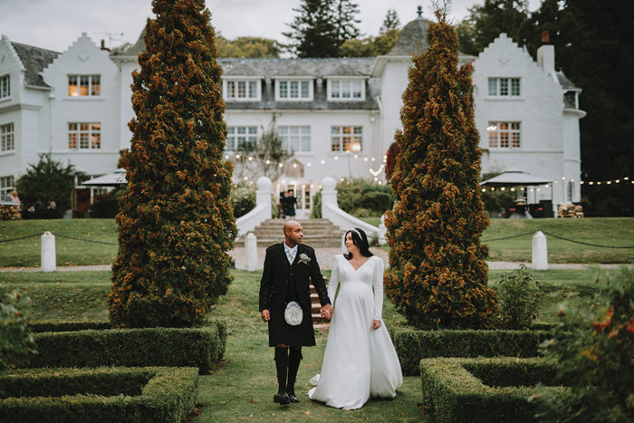 A bride and groom holding hands and walking in a garden at Achnagairn Castle