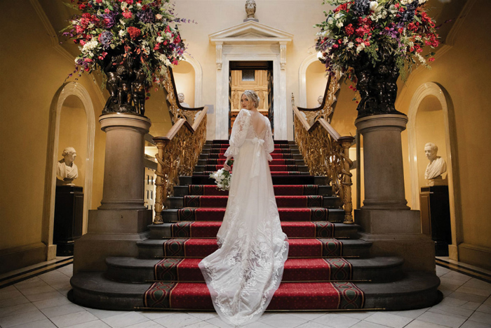 Bride on staircase looking back over her shoulder holding her bouquet 