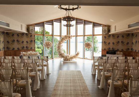c shaped flower display at the top of aisle in front of large windows looking out to a body of water and greenery