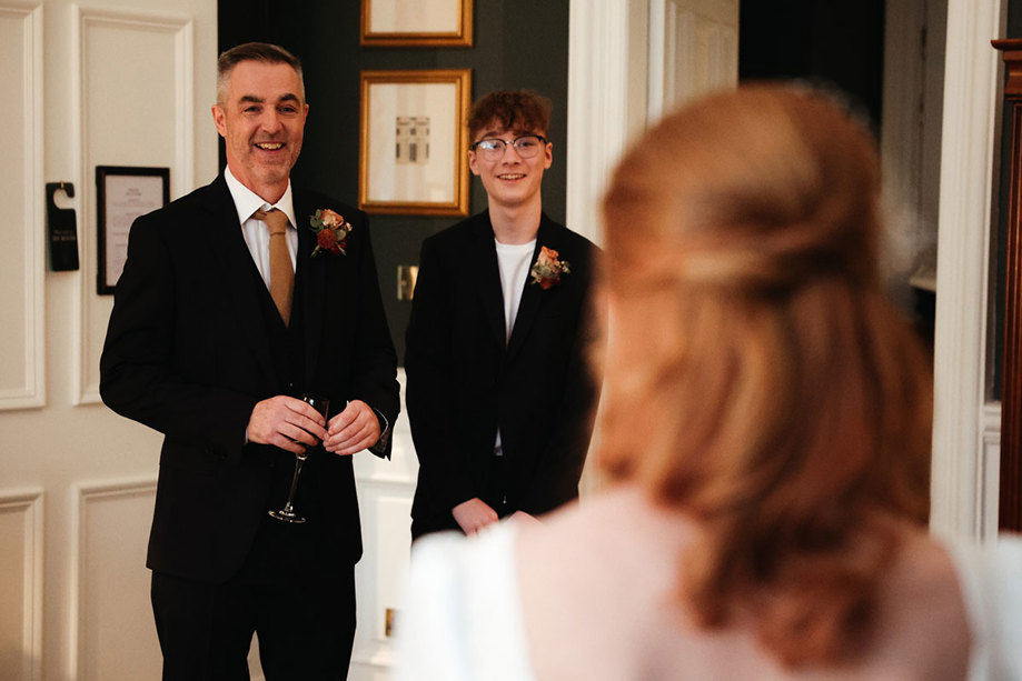 Two men smiling wearing suits looking at a woman with her back to the camera 