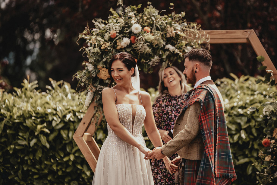 Bride and groom hold hands during the ceremony while bride laughs at guests