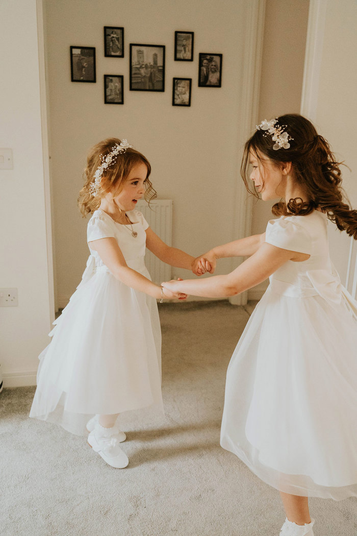 Two girls holding hands in white dresses.