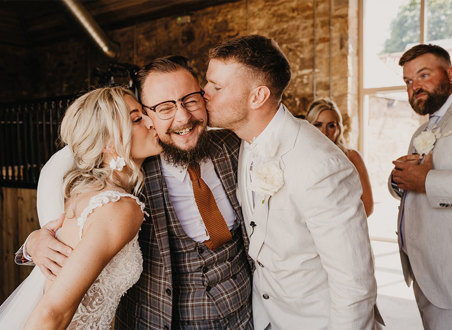 Bride and groom kissing man on cheek