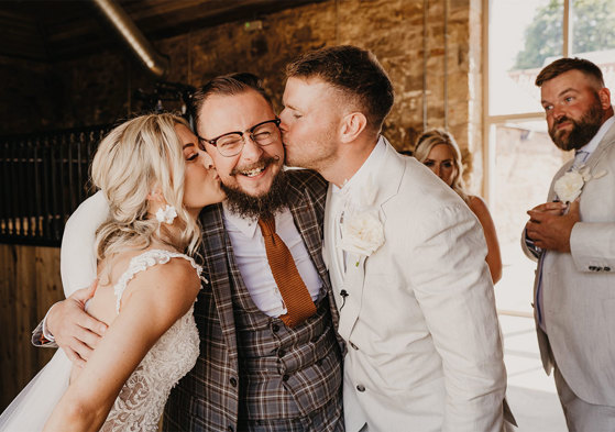 Bride and groom kissing man on cheek