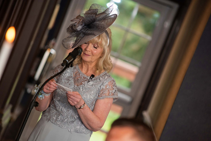 A Person Wearing A Grey Lace Dress And Hat Standing In Front Of A Microphone