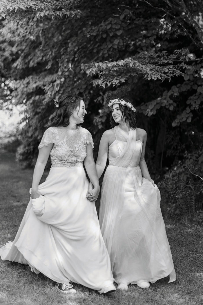 two joyful brides walking across grass below trees at the Byre at Inchyra