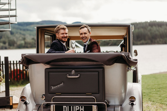 Grooms smile from wedding car that has its roof down