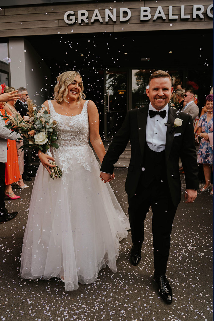 a bride and groom walking while being showered in confetti outside The Redhurst Hotel.