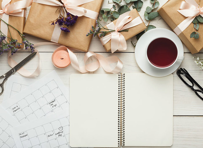 desk with wedding planning set up including calendar, flowers, notebook and tea