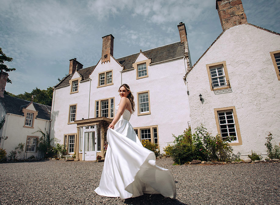 bride in white strapless dress twirls in gravel driveway outside white house