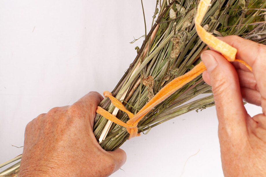 hands tying together stems of dried flowers into bouquet