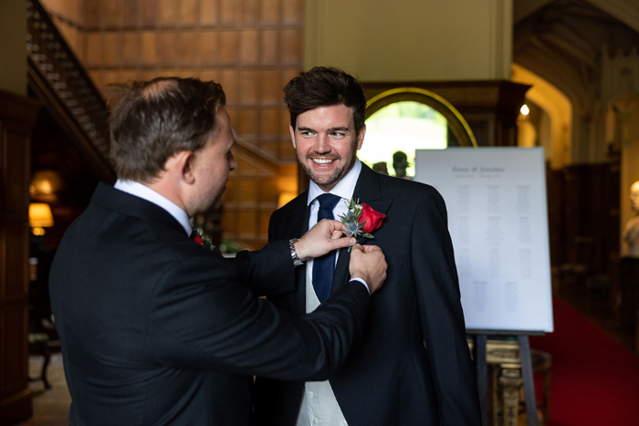 Man fixes red rose buttonhole to groom's lapel 