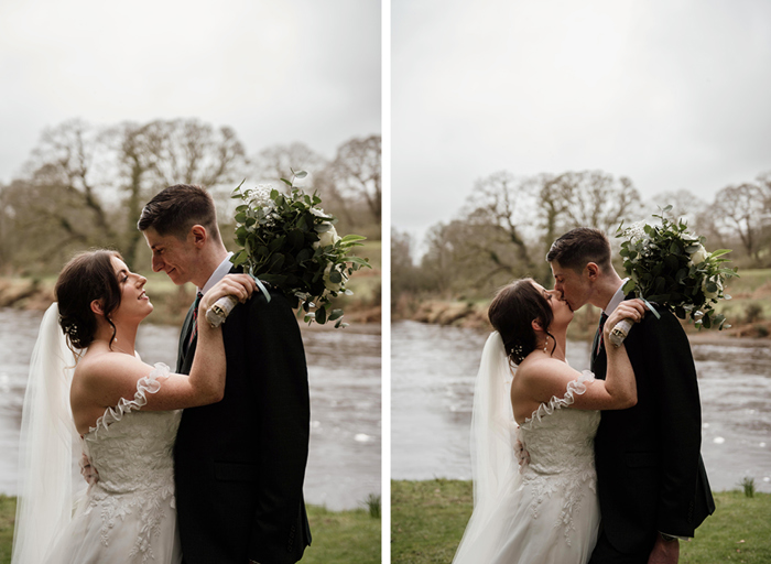 A bride and groom kiss in front of a lake 