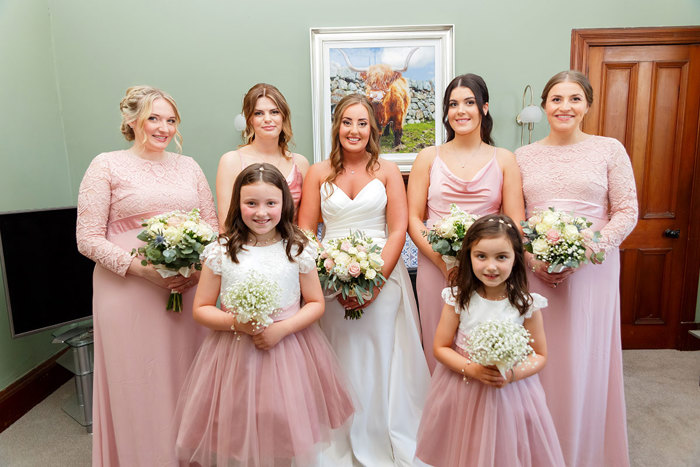 a group of women and girls in long pink dresses with a bride in a white dress in the middle 