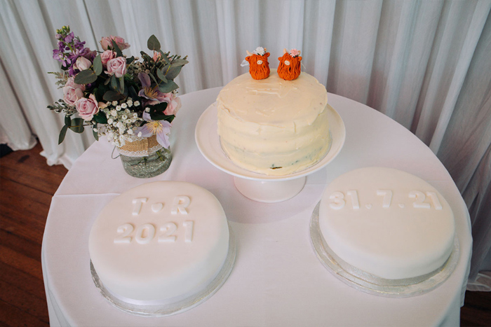 Three White Wedding Cakes On A Round Table With Highland Cow Cake Topper On One