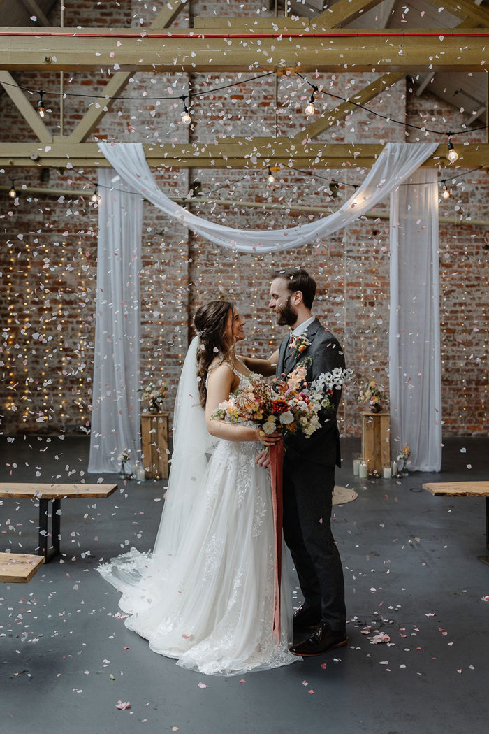 coloured confetti falls around bride and groom stood in a close dance position, both holding onto wildflower bridal bouquet