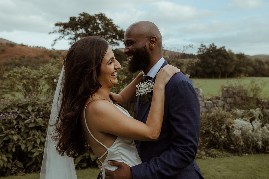 A Bride And Groom Embracing And Laughing With Arran Countryside In Background