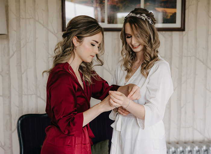 woman in a red silk robe puts a bracelet on the wrist of a women in a white silk robe