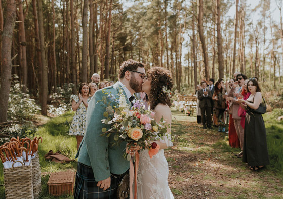 couple kissing after getting married - bride holding colourful floral bouquet