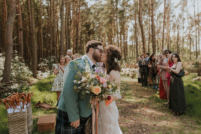 couple kissing after getting married - bride holding colourful floral bouquet