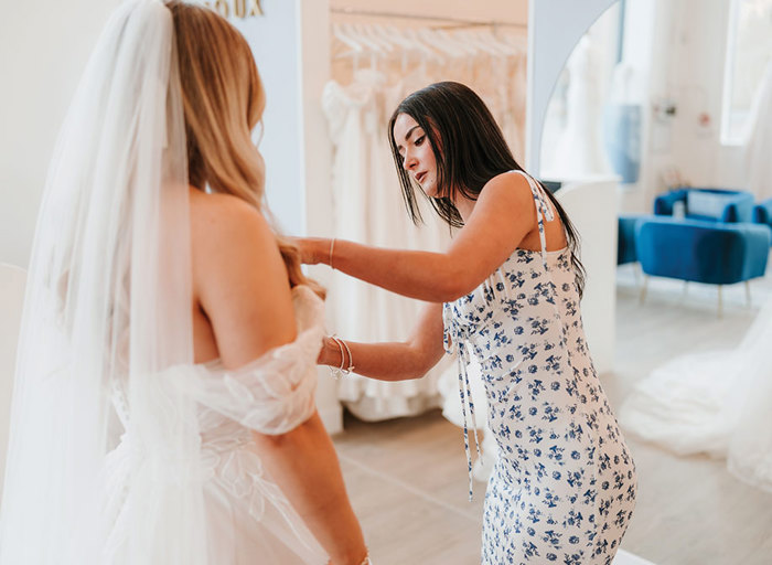 bridal consultant with white dress and blue flowers adjusting brides dress