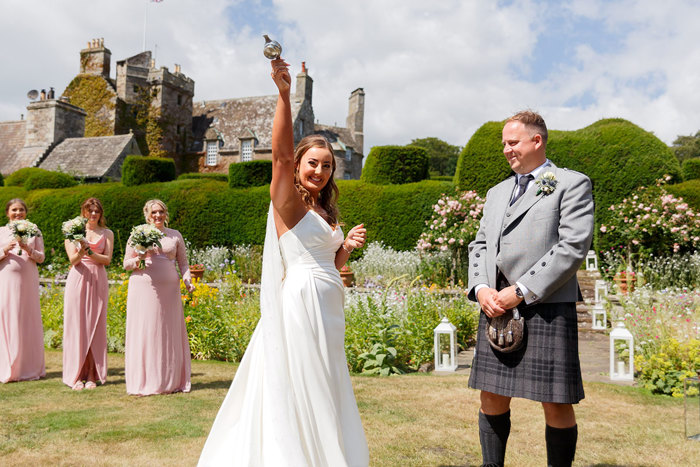 A bride holds a quiach in the sky while the groom and bridesmaids look on