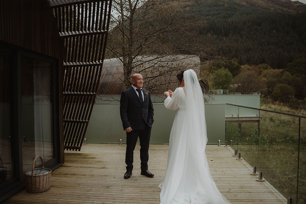 a bride and a man in a suit on a wooden deck with glass panels