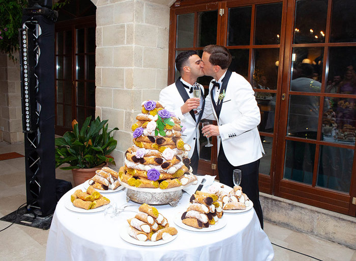 two grooms kissing in front of a table of cannolis