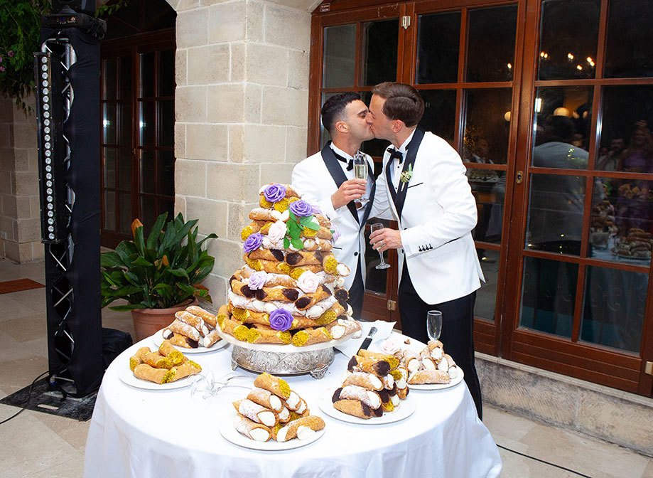 two grooms kissing in front of a table of cannolis