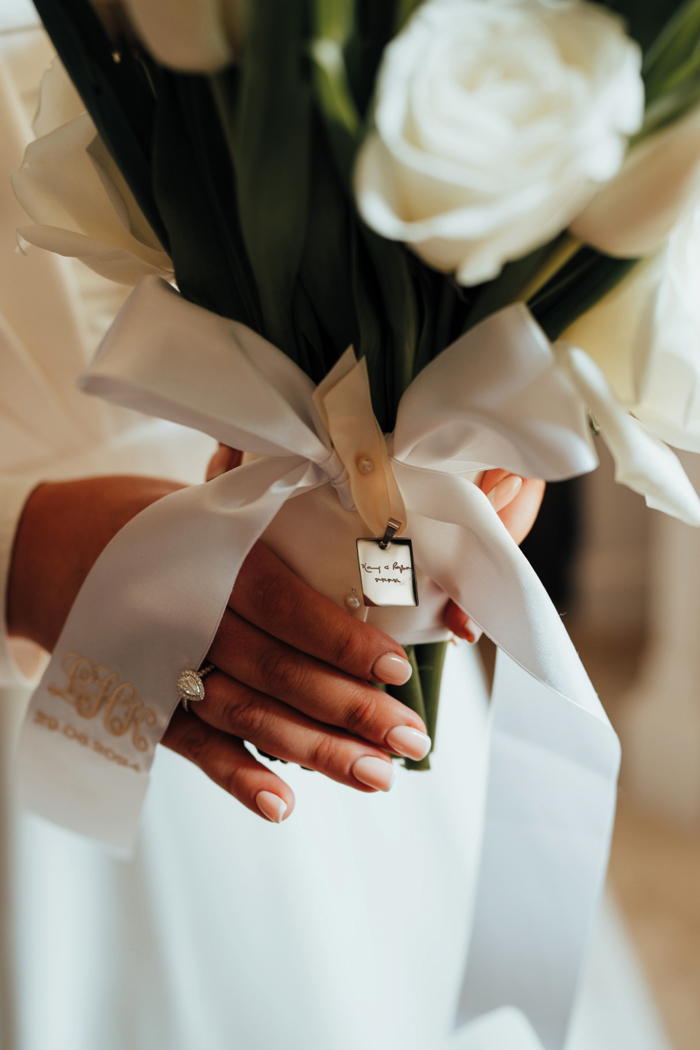 A close up photo of a woman holding a bouquet of white roses tied in a white ribbon