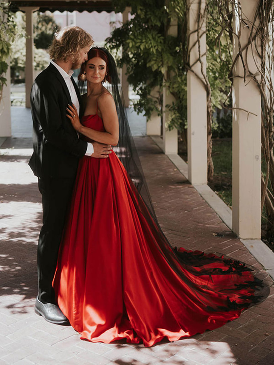 a couple embracing each other as man wears black suit and woman wears black veil and long trailing red dress