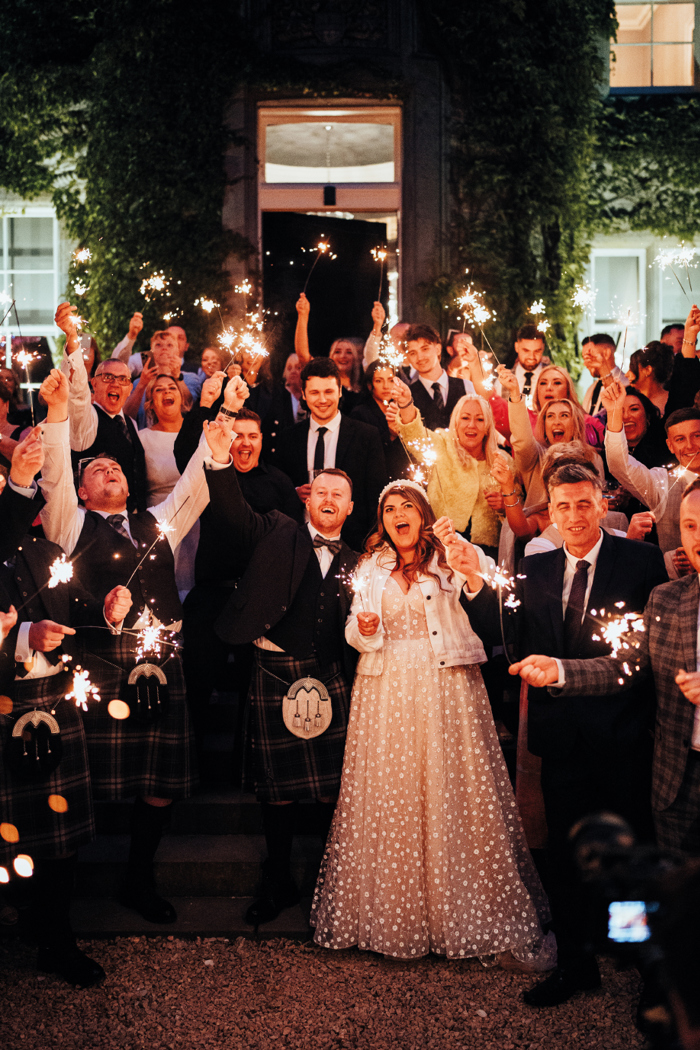 A group of people holding sparklers and standing on a staircase in front of a doorway