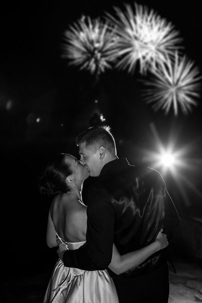 A bride and groom kissing in front of fireworks.