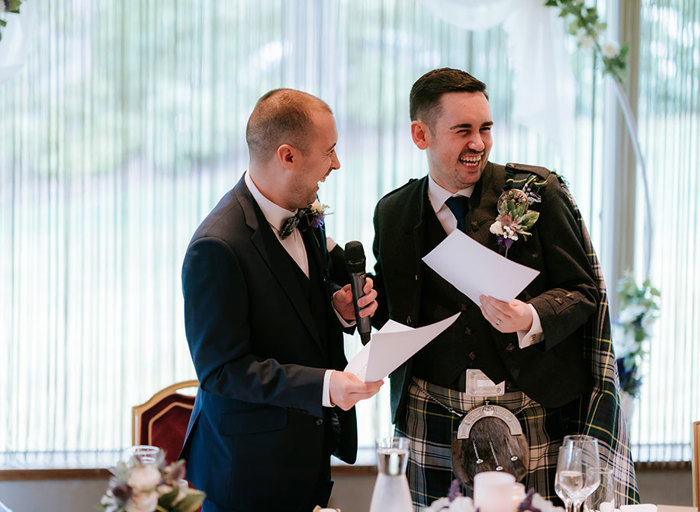 two grooms laughing as they make wedding speeches