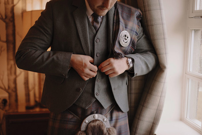 shoulder down image of man in full green tonal kilt outfit as he buttons his waist coat