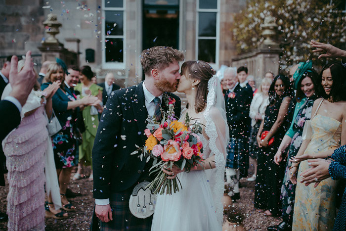 a bride and groom kissing outside Netherbyres House as guests shower them in confetti