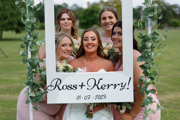 five women stand together in front of a selfie board that says 'Ross + Kerry! 01.07.2023' 