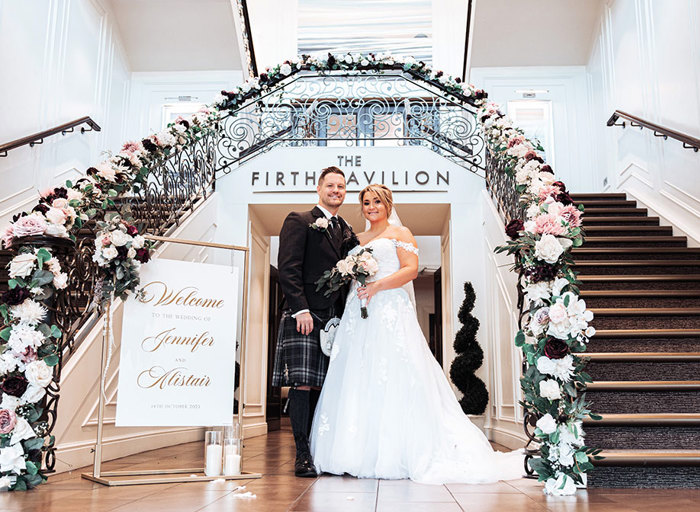 bride and groom at ceremony surrounded by a decor sign, flowers and staircases