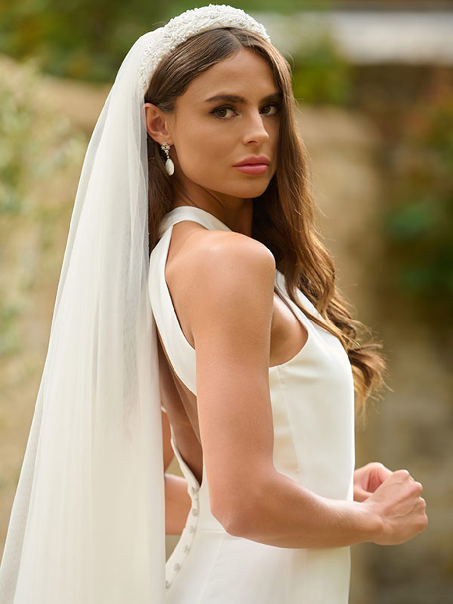 a close up image of a brunette woman wearing a white gown and long veil stemming from a beaded headband